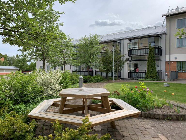 Parkbänk vid grönyta mellan lägenhetshus